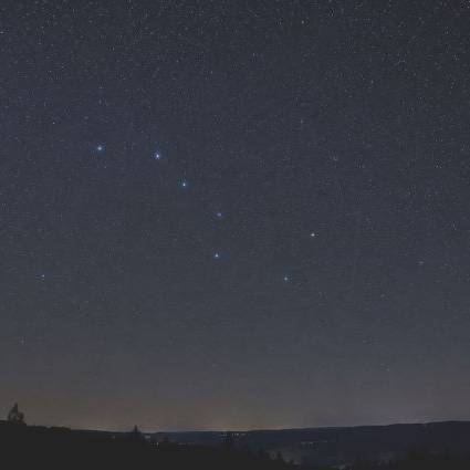 Ein Sternenhimmel mit sichtbarer Konstellation über einer dunklen Berggrenze.